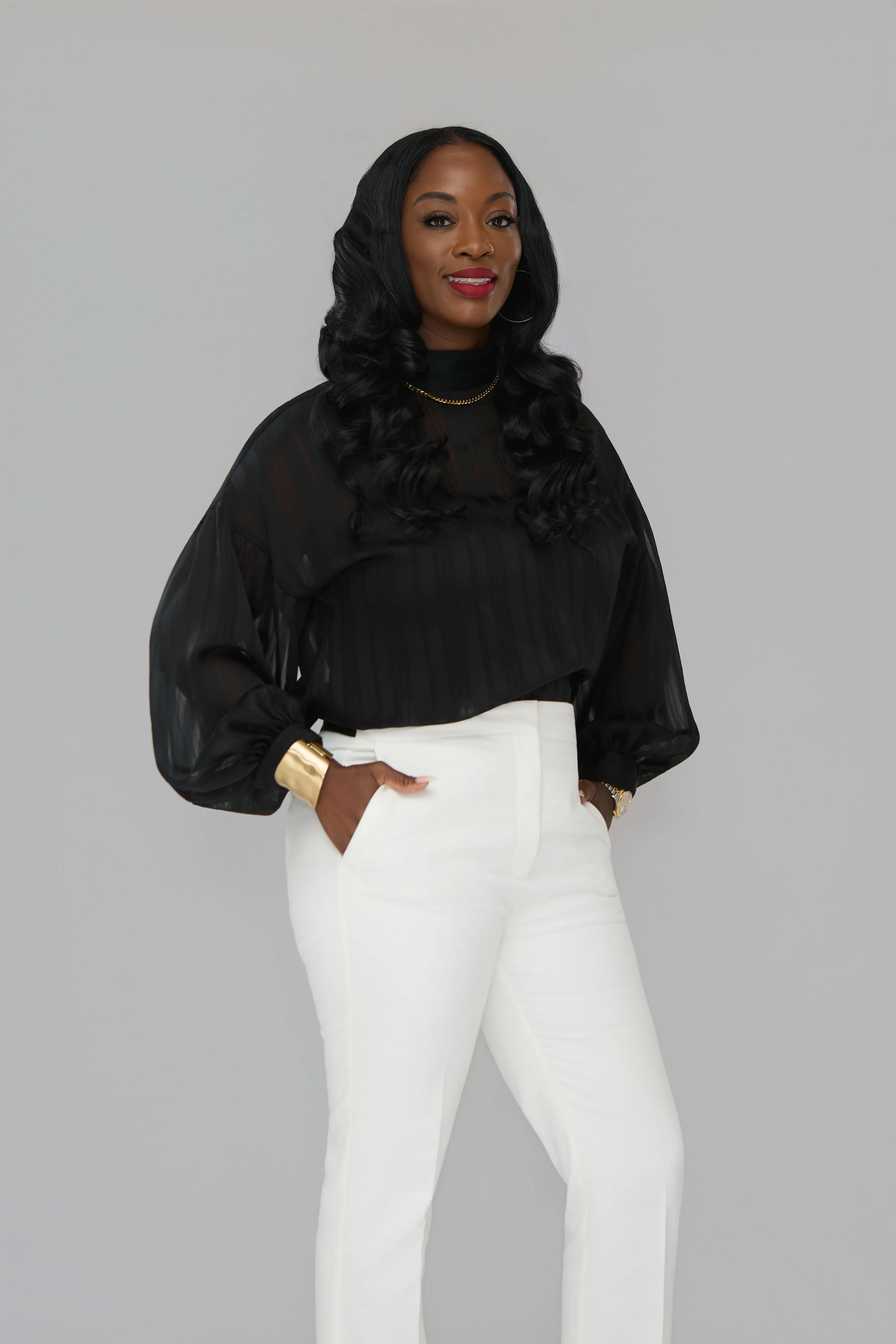 Dr. Syreeta McClain in a black blouse and white trousers against a grey seamless backdrop.